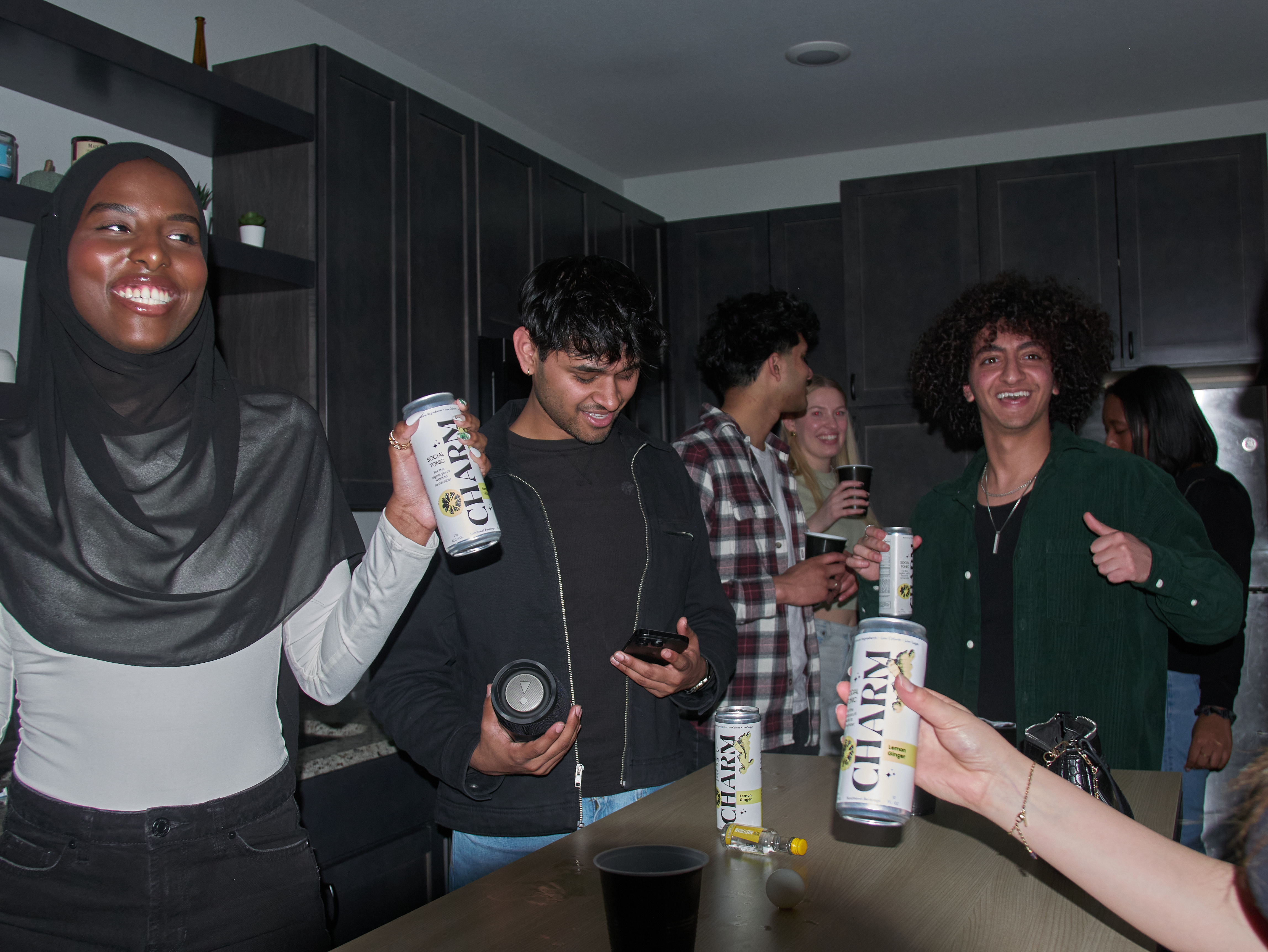 Group of friends standing around a kitchen island with cans of charm and black plastic cups