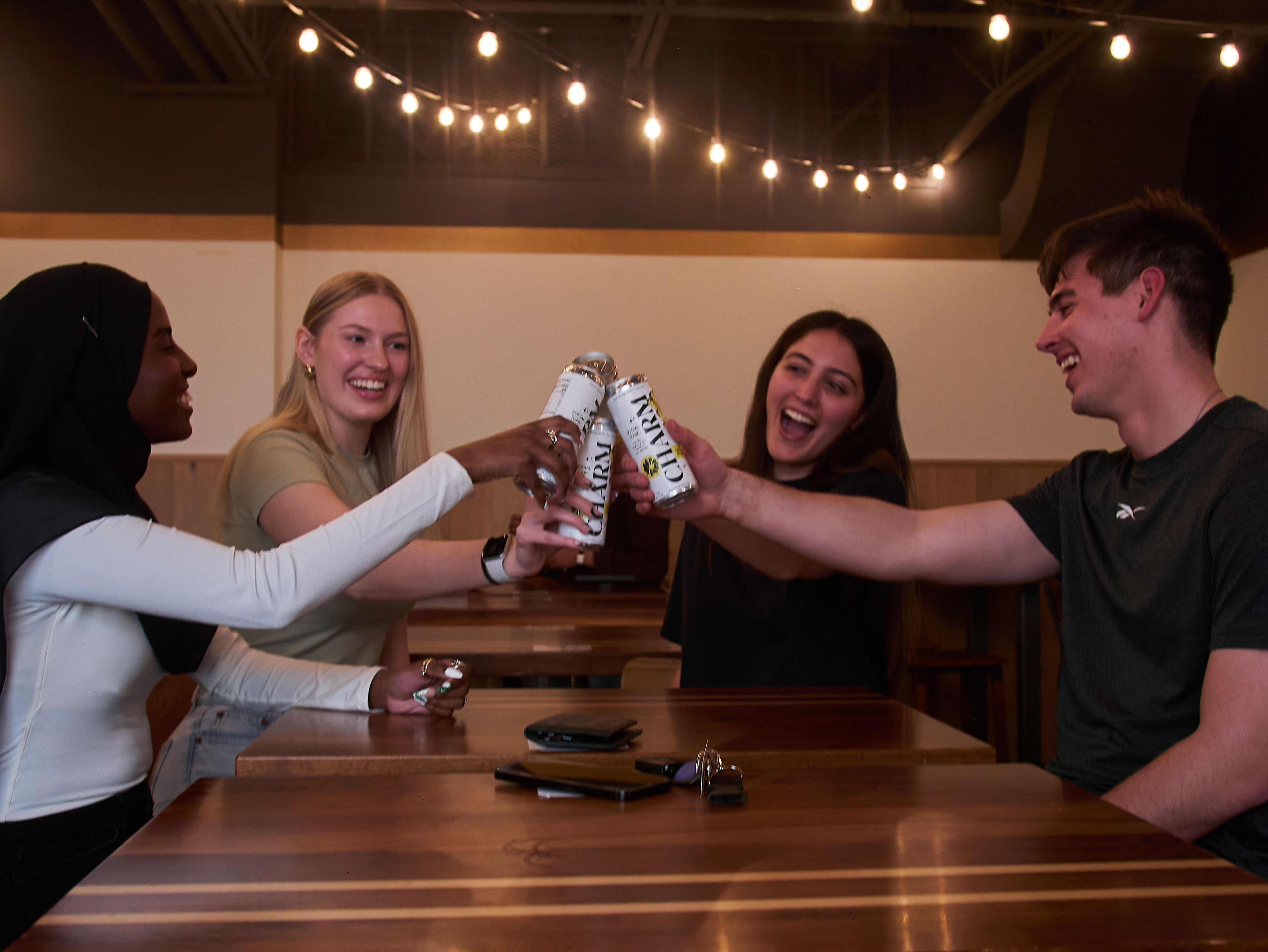 Group of four friends all cheersing with cans of charm